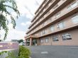 鉄筋コンクリート造りの7階建ての建物。階段のような形で、茶色の外壁が落ち着いた印象を与える。施設の前は駐車場になっている。