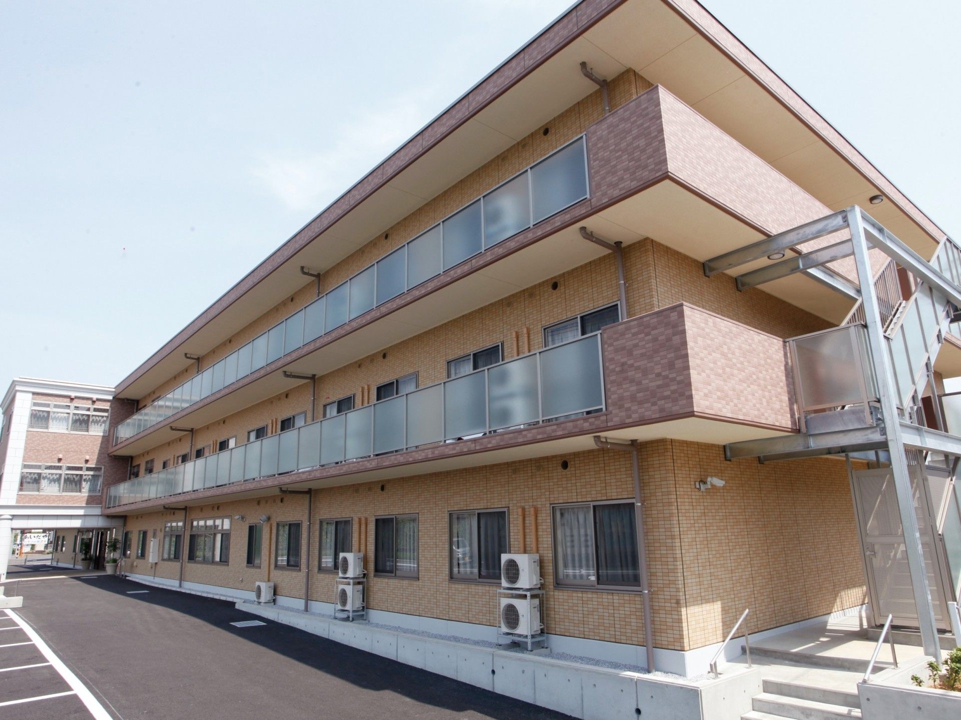 正面玄関から見て建物左端を捉えた外観。職員出入り口が設けてあり、職員駐車場がある。夜間の出入り口もある。