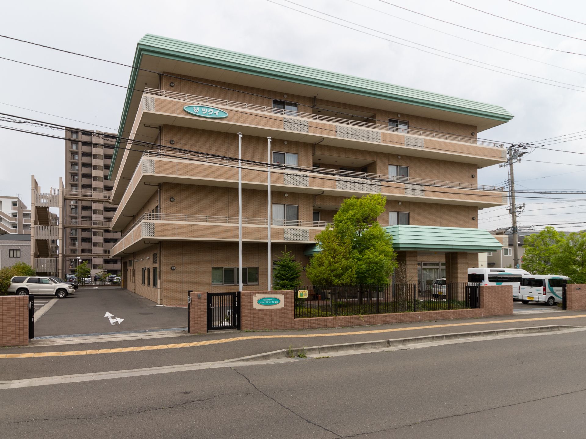 4階建の施設は、外壁がベージュ色のレンガ調で緑の屋根をした建物である。建物前と横に駐車場が設けてある。