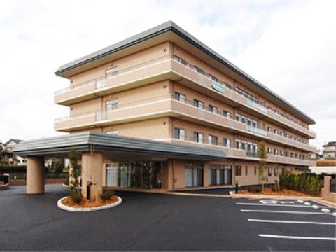 外壁がベージュ、屋根がグリーンの４階建ての建物である。玄関の前に駐車場が広がっていて、玄関から奥に建物が長く伸びている。