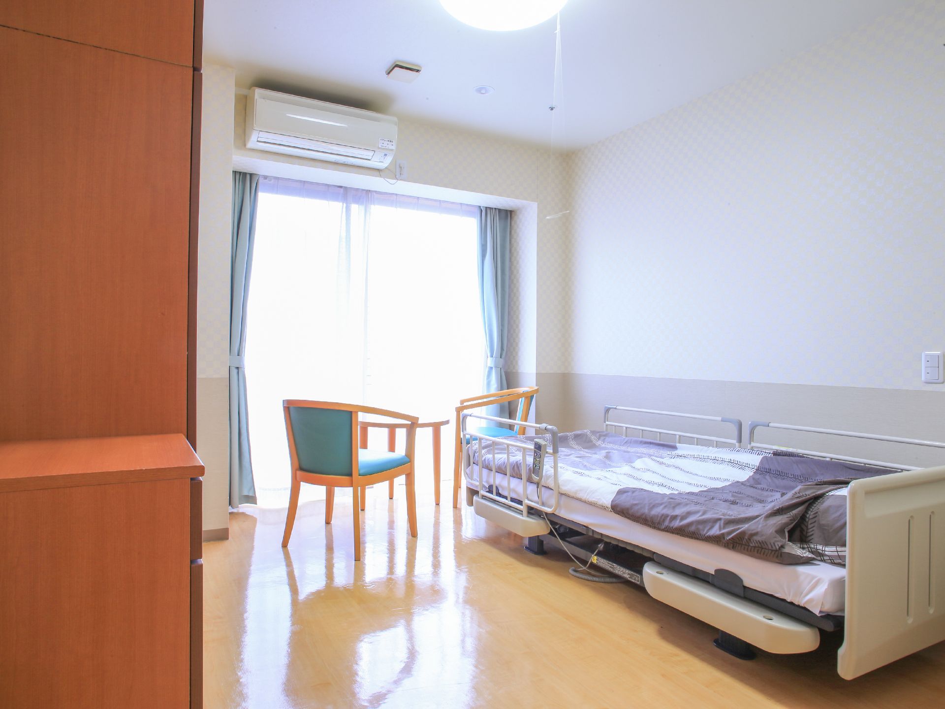 完全個室で、電動のリクライニングベッド、エアコン、収納家具、2人掛けのテーブルセットが標準装備されている。身の回りの物を揃えれば入居できる。