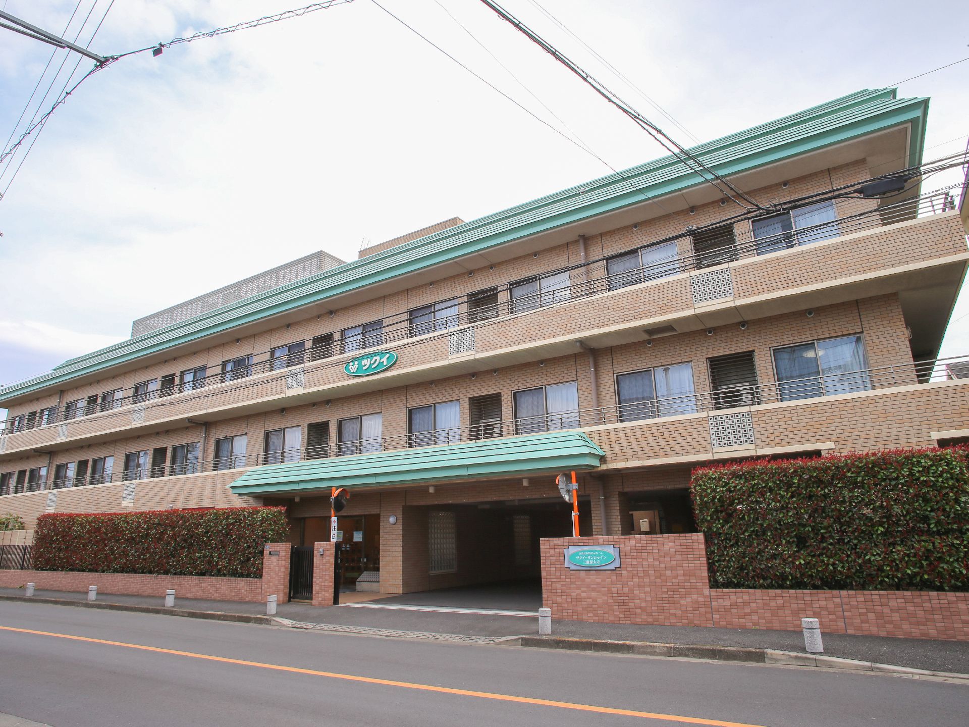 建物はオレンジのレンガ調の壁とグリーンの屋根の3階建て、ピロティ形式で1階に駐車場があるため、雨の日でも車の乗降時に濡れる心配がない。