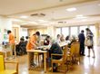 食事の様子。15名くらいの方が席についている。職員がお茶を入れて利用者さんが手伝おうとしているように見える。