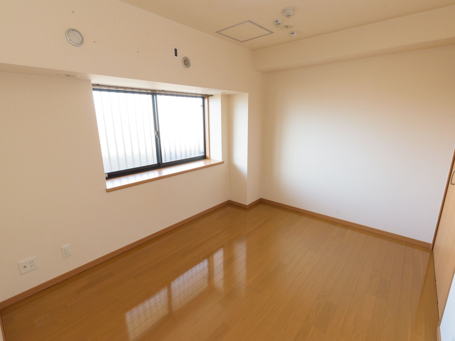 要介護のお一人様用居室は、明るい日が注ぐ大きな窓があり、床はバリアフリー。見守りセンサーが天井に設置され、壁の上部には空調穴がある。