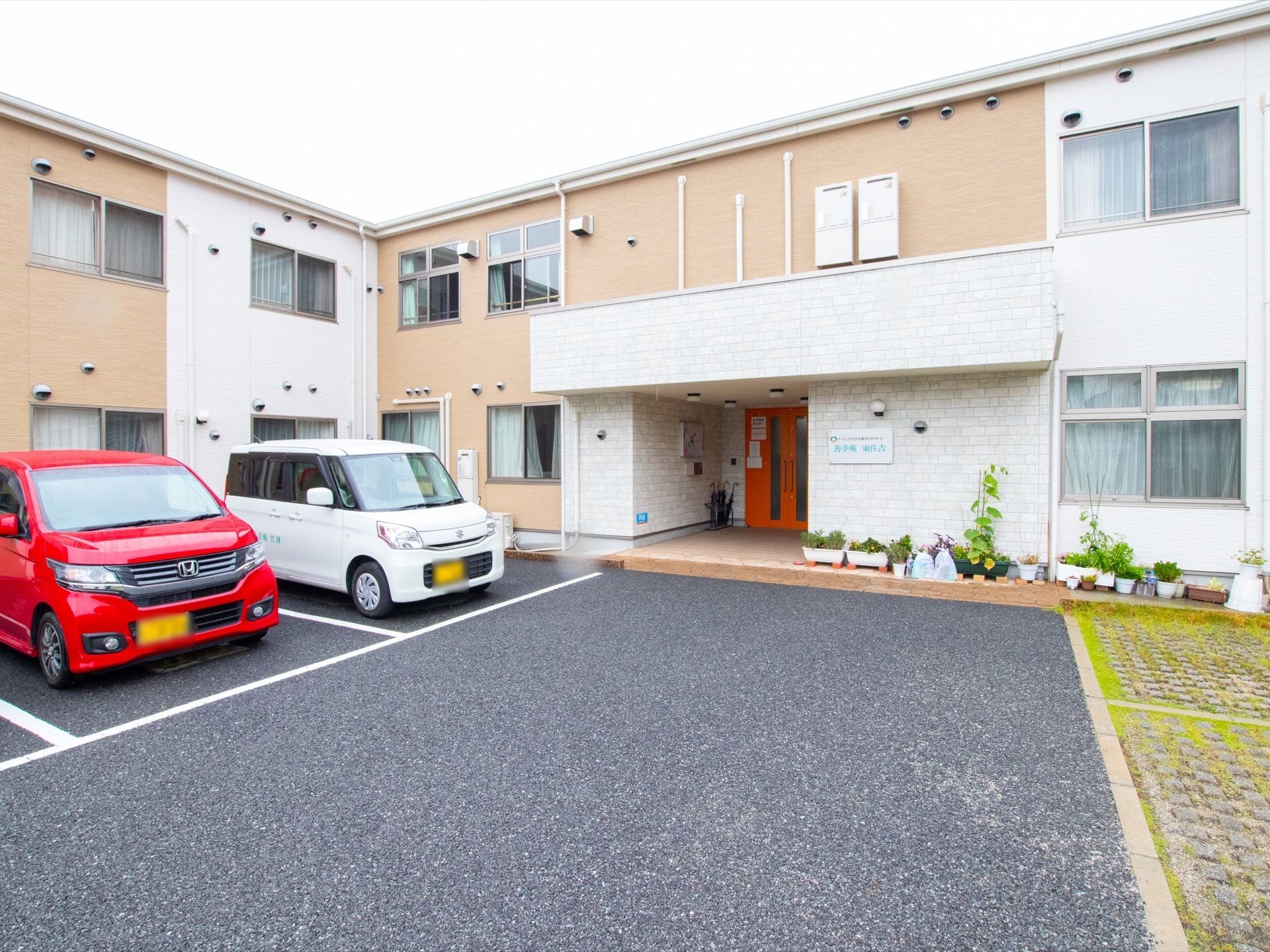 建物の前方は駐車場になっており、左側はアスファルト舗装されているが、右側は芝生のような草が生えた地面になっている。