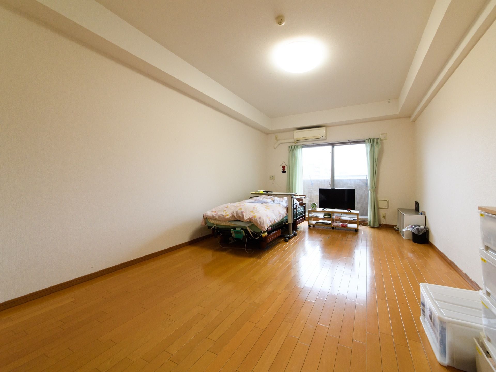 ベッドやテレビがある居室は明るく広々としている。窓が大きく薄い緑色のカーテンが掛けられている。ベッドには転落防止の柵が取り付けられている。
