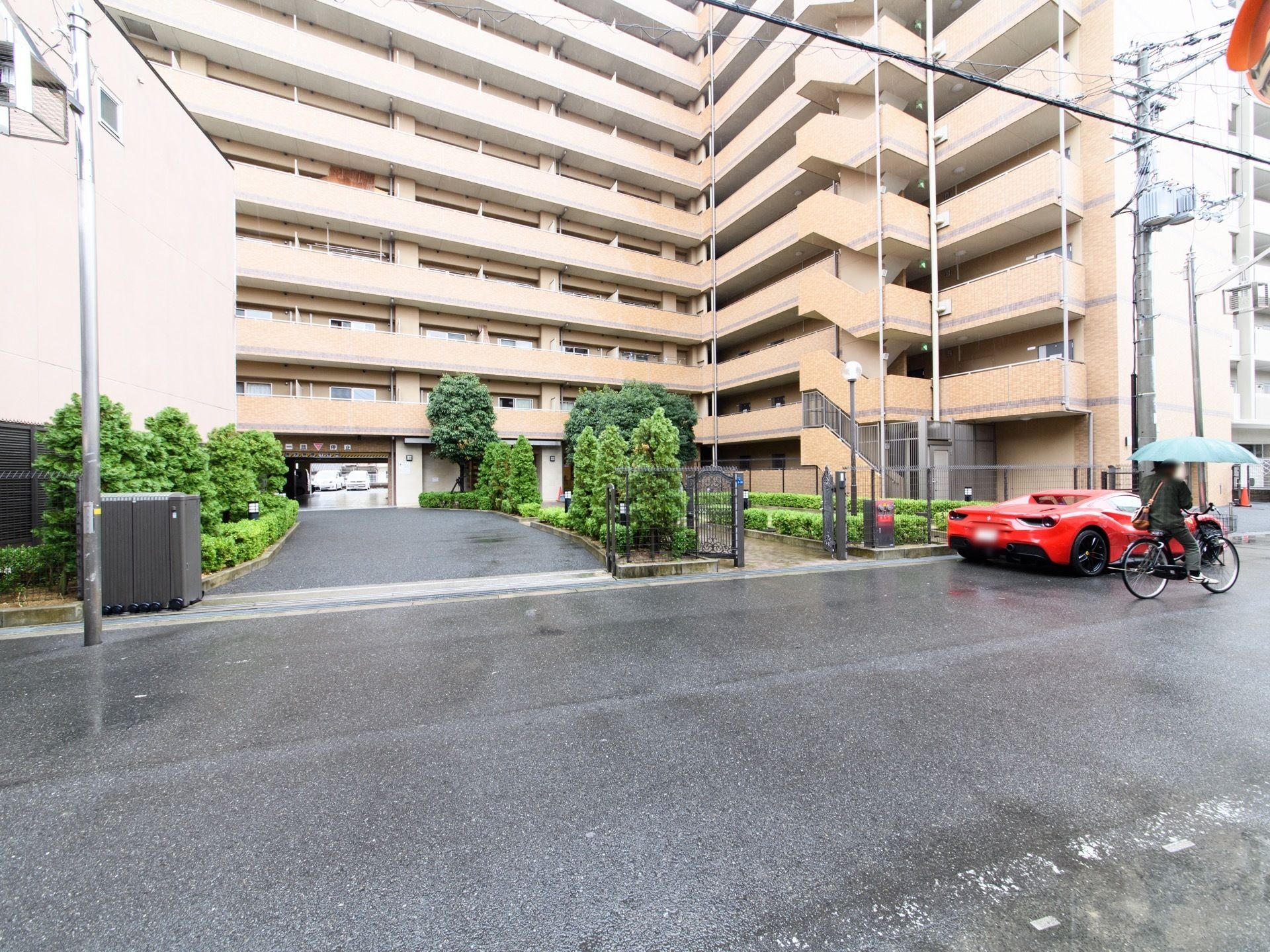 巨大なマンションのような建物である。建物をくぐって向こう側に駐車場が設置されている。木々が敷地内にたくさん植えられている。