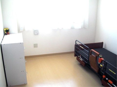 窓からの日差しが明るい、個室タイプの居室である。スペースに余裕があり、ベッド、収納家具、カーテンがあらかじめ設置されている。