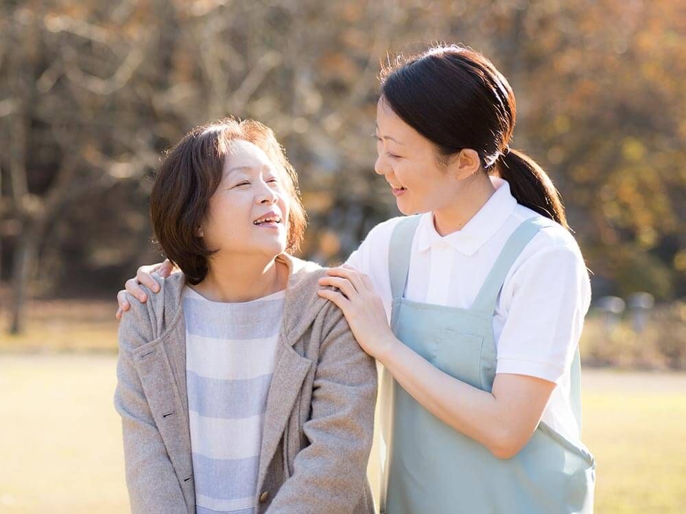 夕日に目を細める高齢女性と介助をする女性ヘルパー