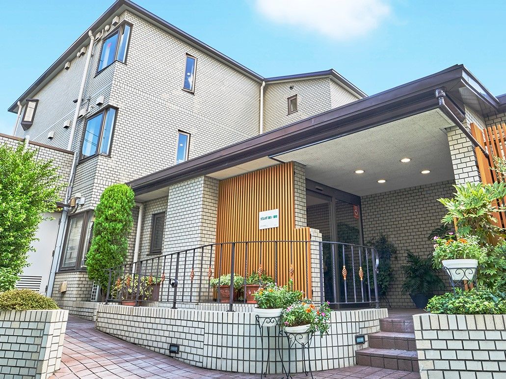両サイドに植栽が施された、ベージュ系の3階建ての施設外観