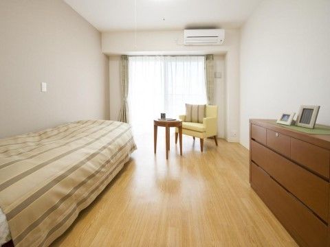 壁を白で統一した落ち着きのある居室となっている。壁際にベッドがあり、１人掛けのソファとテーブルが用意されている。