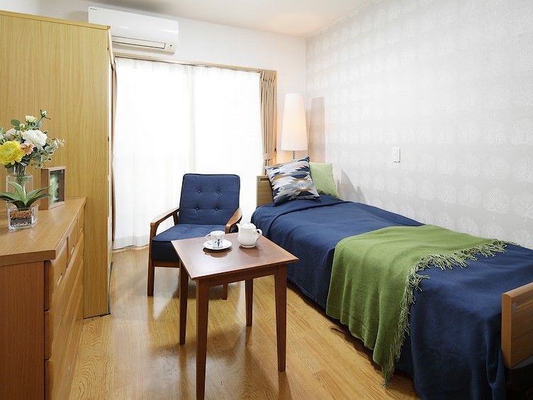 白い壁に木調の床のシンプルな部屋に家具が配置されている。大きな窓の上には自由に温度調節できるエアコンも完備している。