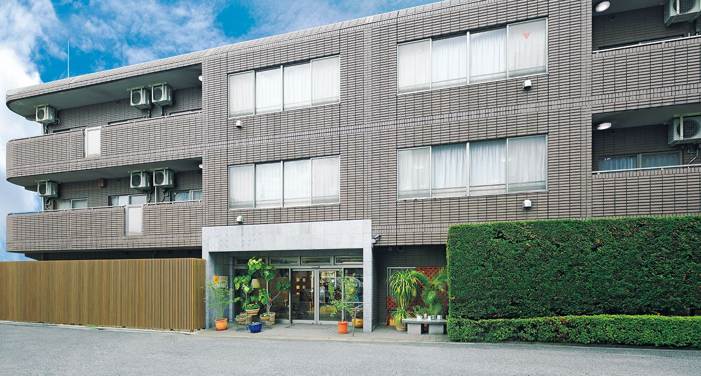 落ち着いたブラウンの壁である。3階建ての建物で、エントランスはバリアフリー構造である。建物のまわりには木々が植えられている。
