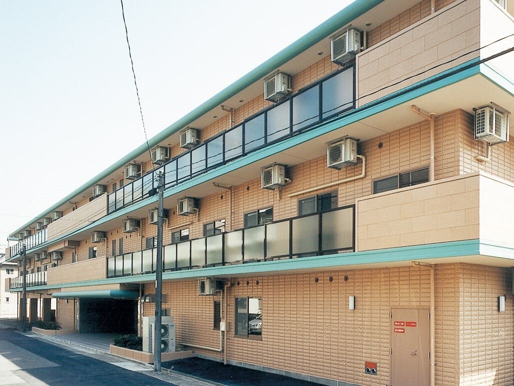 オレンジのレンガ調の外壁とグリーンのラインが印象的な3階建ての施設。各お部屋には窓とベランダがあり、開放的である。