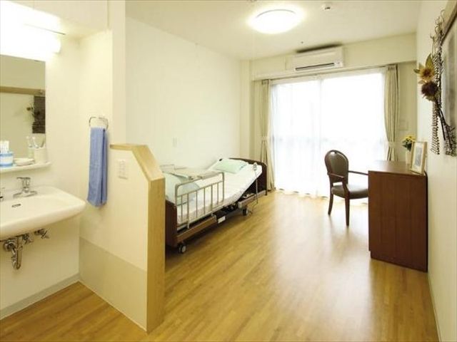 介護用ベッドや落ち着いた色調の調度、使いやすい洗面台が配置された居室