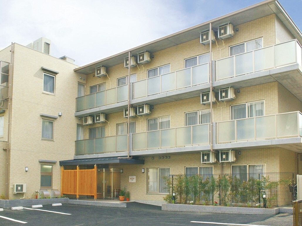 住宅街の中にある三階建ての建物である。前に駐車スペースが設けられており、入口の横に植物が栽培されている。