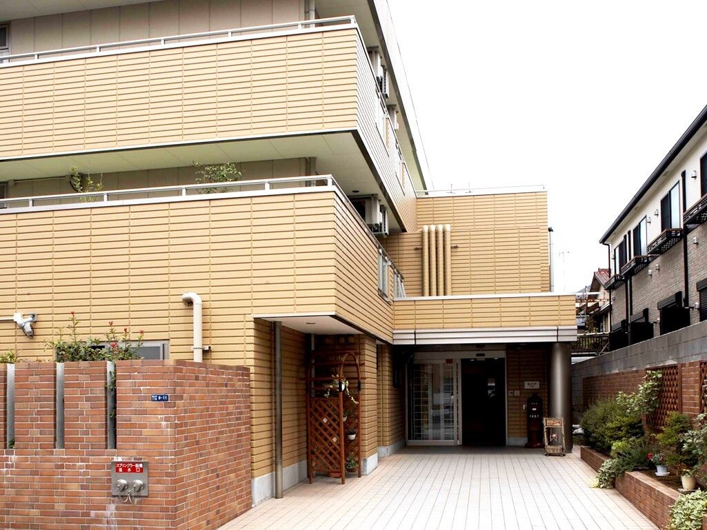 玄関アプローチの横にレンガ調の花壇が設けられている、3階建ての施設外観