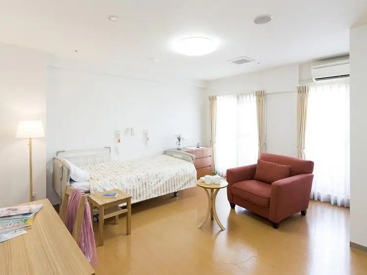 掃き出し窓が２つあり、横にはエアコンが設置されている。ベッド、チェスト、一人掛けソファ、デスク、間接照明を配置しても余裕のある広さである。