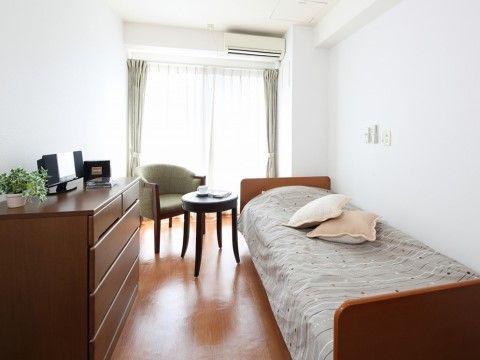 居室には布団がセットされたベッド、テーブル、椅子が置かれている。5つの収納スペースがある洋服ダンスも用意されている。
