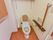 居室に完備されているトイレである。温水洗浄便座器で、手すりや背もたれパッドが設置されており、安全である。