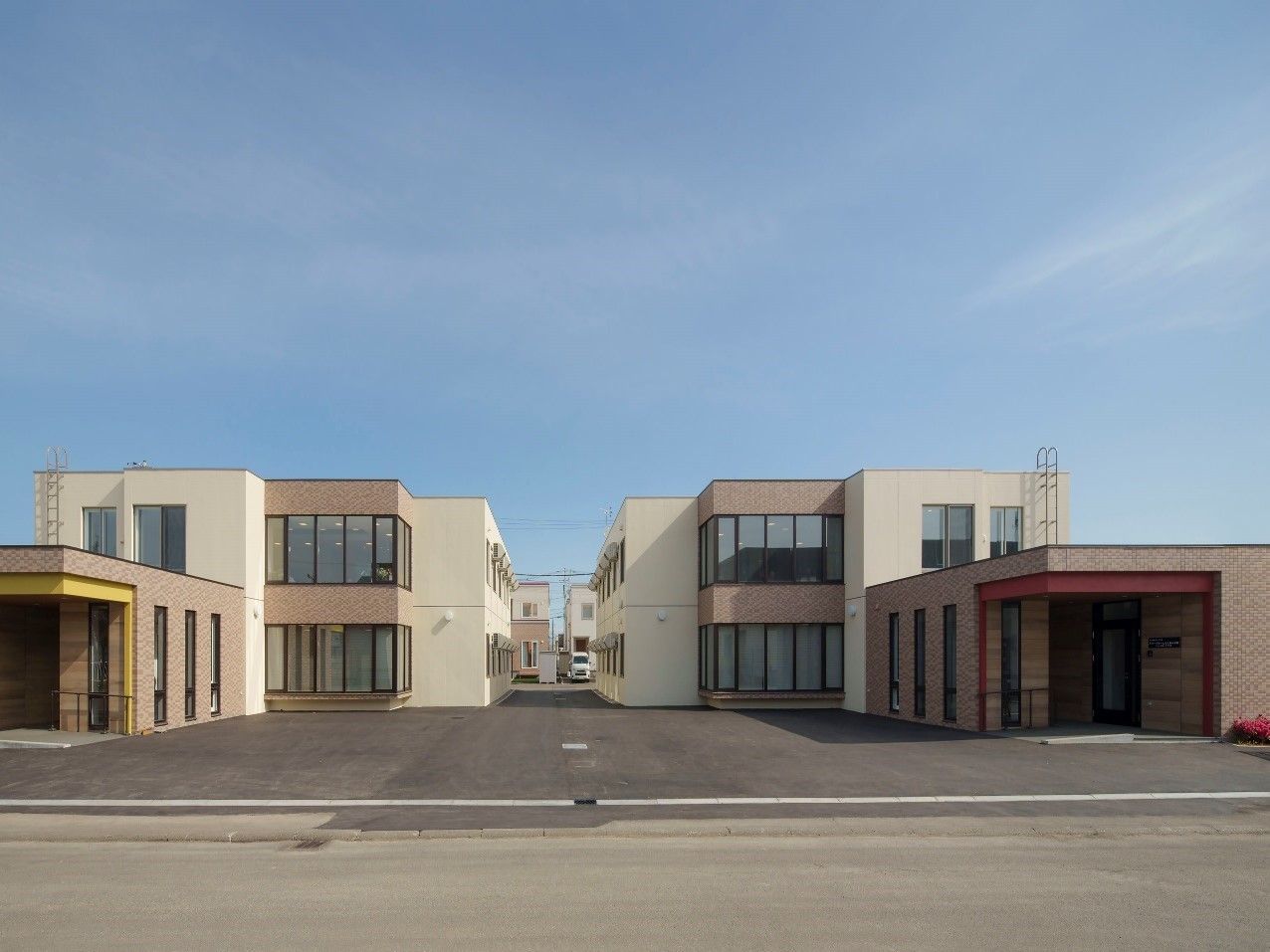 グレー系の建物は一部2階建て、一部1階建てで道路に面していて、建物の敷地内には車も止められている。