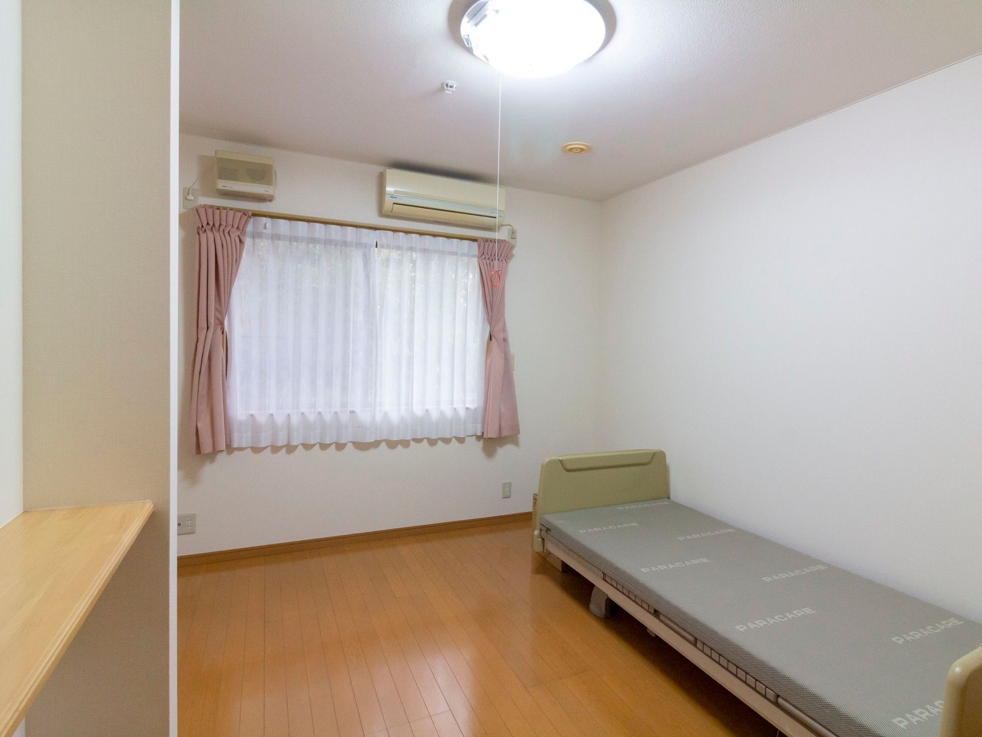 居室にはレースとカラーカーテンがかけられた窓がある。エアコンが完備されており、ベッドも用意されている。
