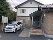 居住部分とデイサービスは別の建物で、エントランスの通路でつながる形になっている。タイル調のおしゃれな外観で、敷地内に送迎車が停められている。