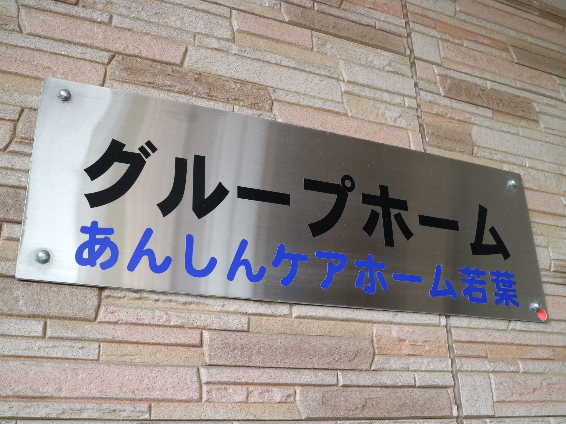 エントランスの外壁には、メタリックの板に太く大きな文字で施設名が明記されている。デイサービスと区別のため、グループホームの文字も入っている。