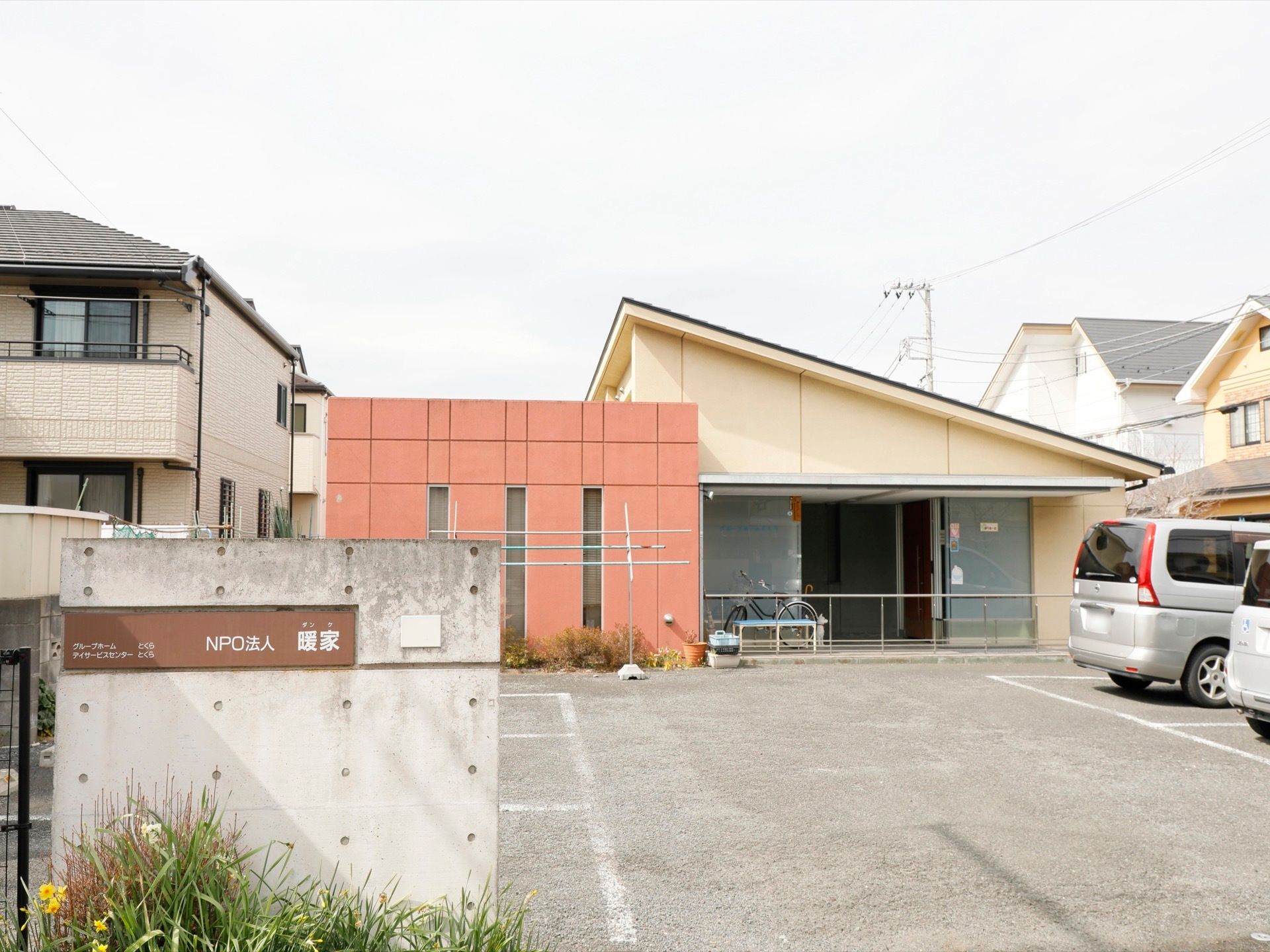 敷地境界に立っているコンクリート塀に、茶色地に白色の文字で施設名称の書かれた看板が設置されている。敷地内に駐車スペースがある。