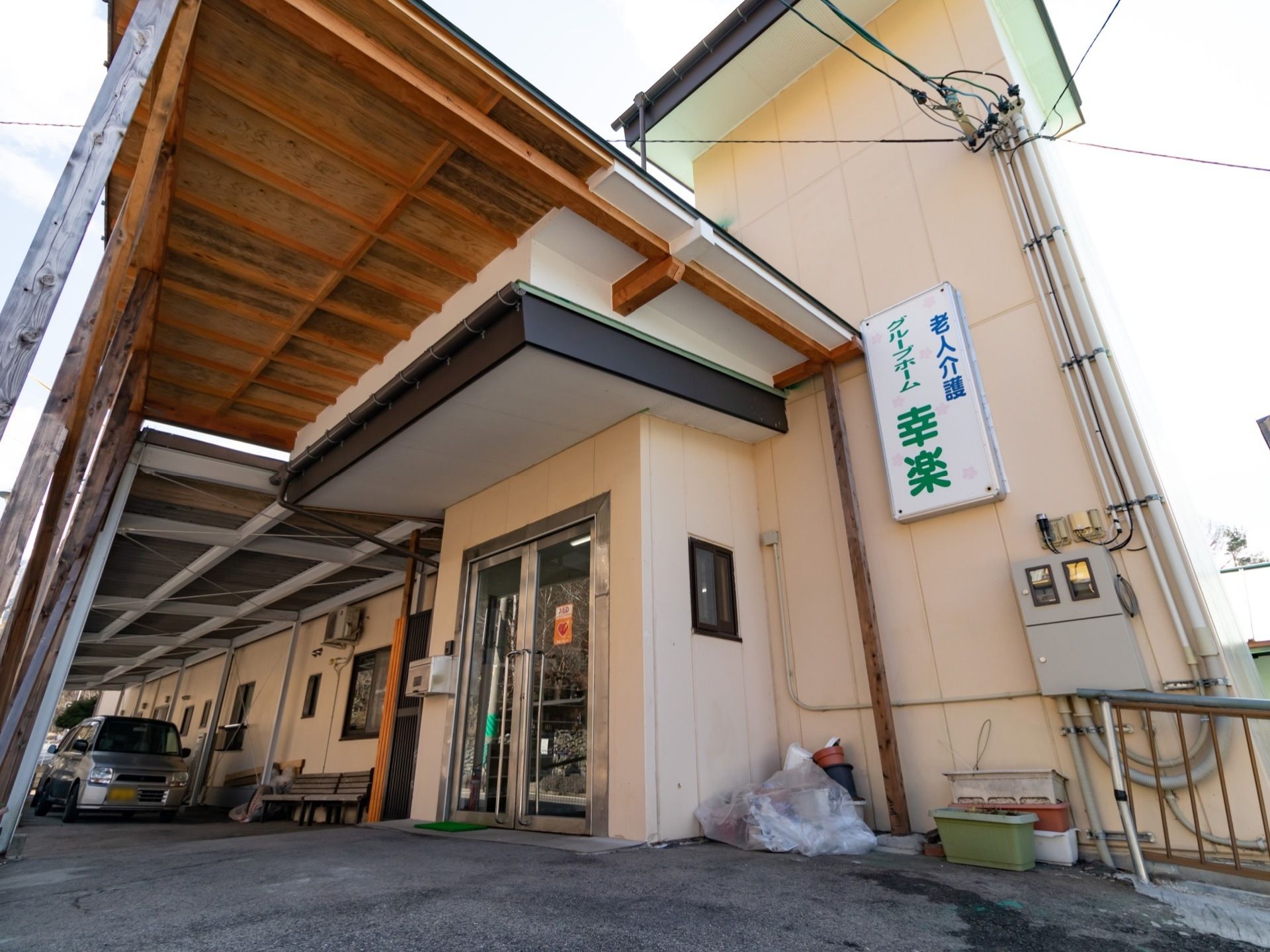 淡いクリームカラーの施設外観になっている。外壁には施設名が記された看板が設置されている。自動車が1台停まっている。