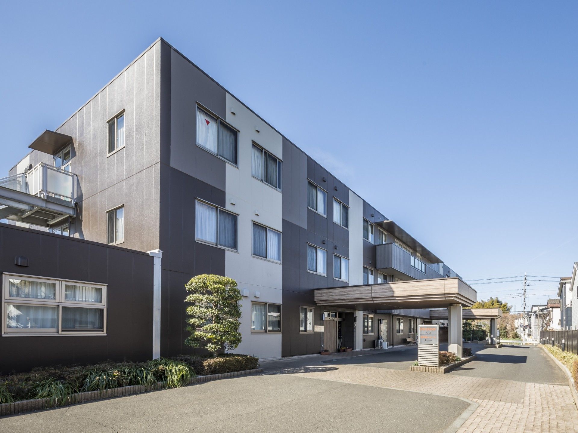 3階建ての建物。入所者の個室の窓には網戸がついており、窓を開けて外からの風を入れることができる。玄関前には施設の車が並んでいる。