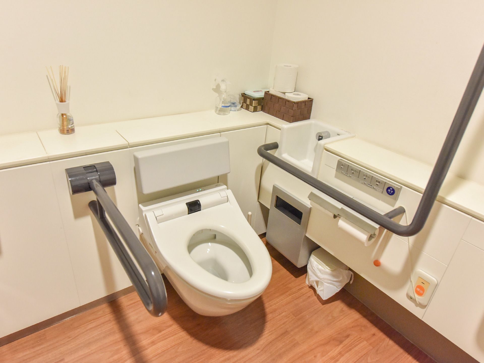白を基調とした清潔感のある機能的なトイレ。便器、手洗い、手すり、ゴミ箱がコンパクトに配置された、使い勝手がよい造り。