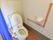 トイレには青いカーテンが掛かっている。壁側にはL字型の手すりが取り付けられている。呼び出しボタンも付いている。