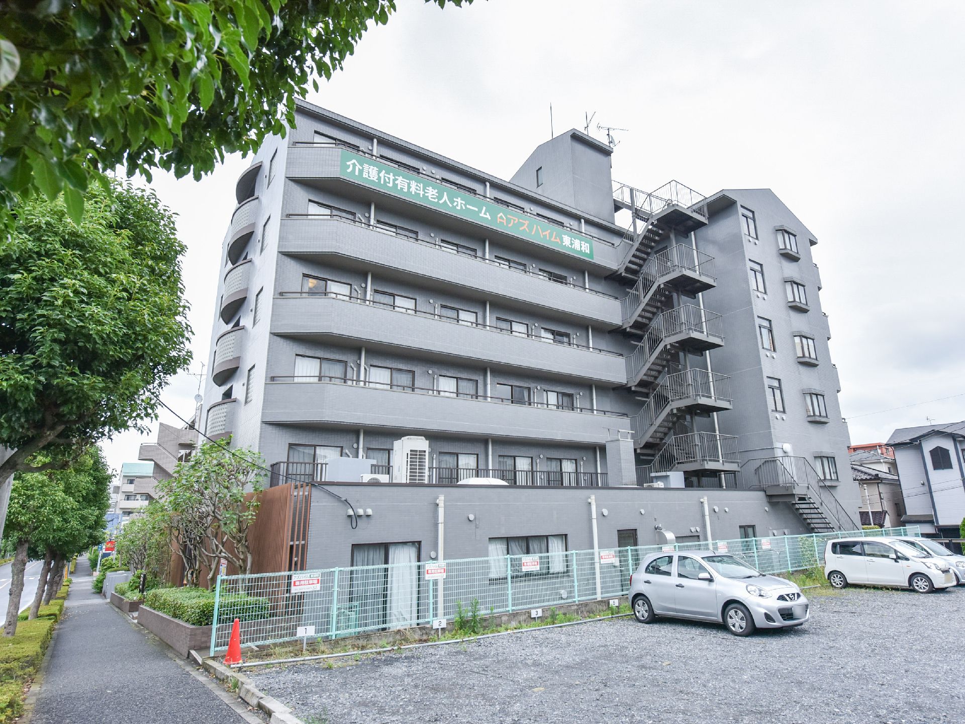 建物は6台建てになっている。6階部分のベランダ部分の外壁には施設名の旗が貼り付けられている。隣は車の駐車スペースとなっている。