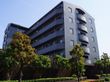 建物は6階建てになっていて、玄関周りは植え込みになっている。施設の隣は車の駐車スペースになっている。