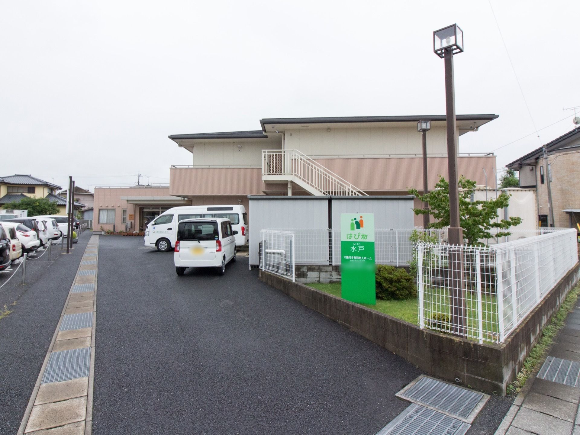 整備された緑地にグリーンの施設看板、外灯が設置されている。まわりには白色のフェンスが備えつけられている。