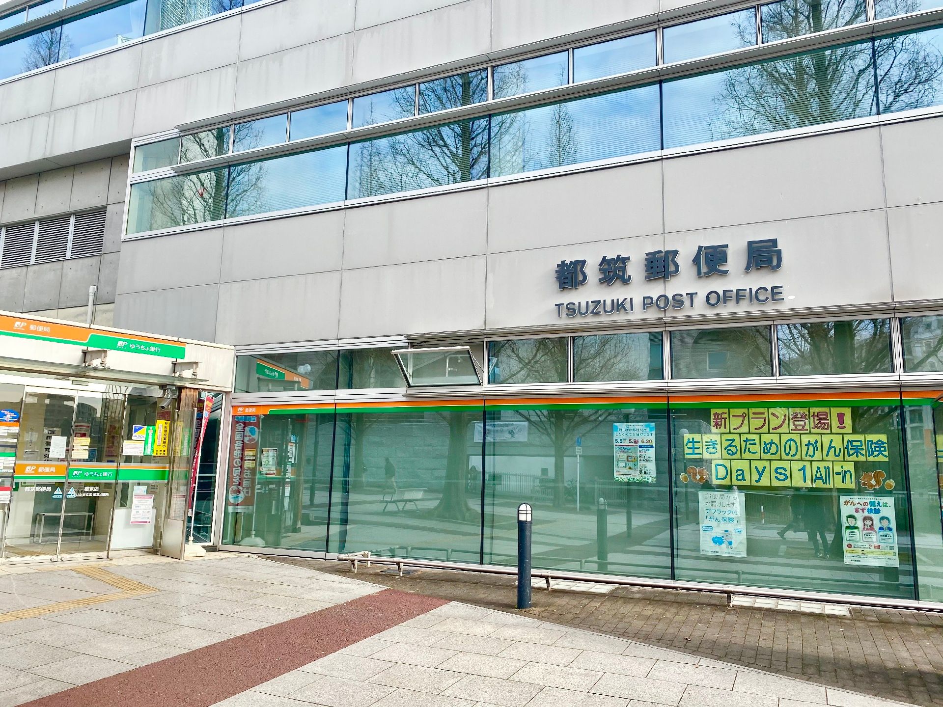 施設近くの３階建ての郵便局。銀行の前には道路に沿って長い駐輪場が設置されている。また、入口に段差はない造りである。
