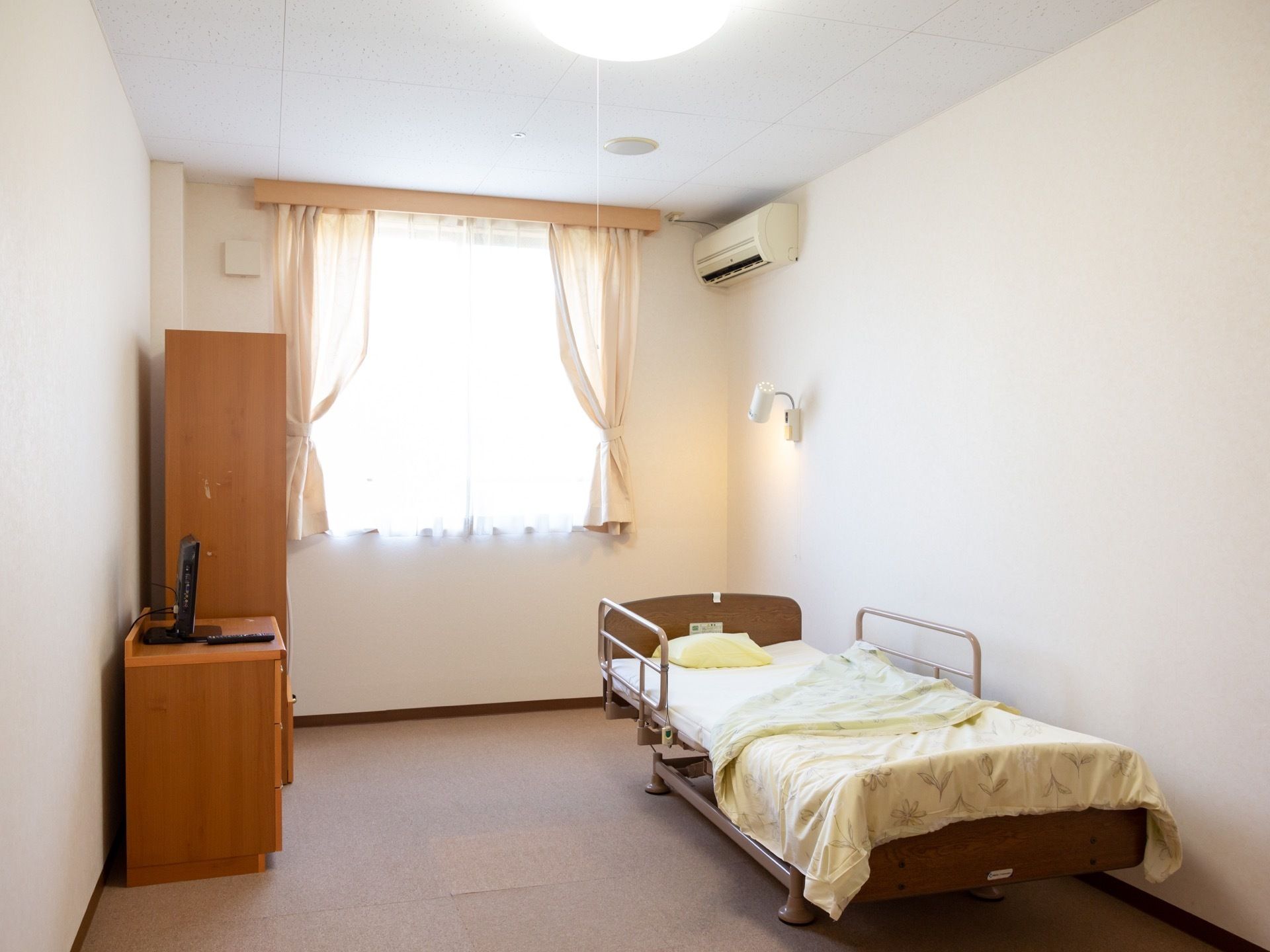 介護用ベッド、収納、ダウンライトなどが完備されている。室内を明るくしている窓には、カーテンがかかっている。