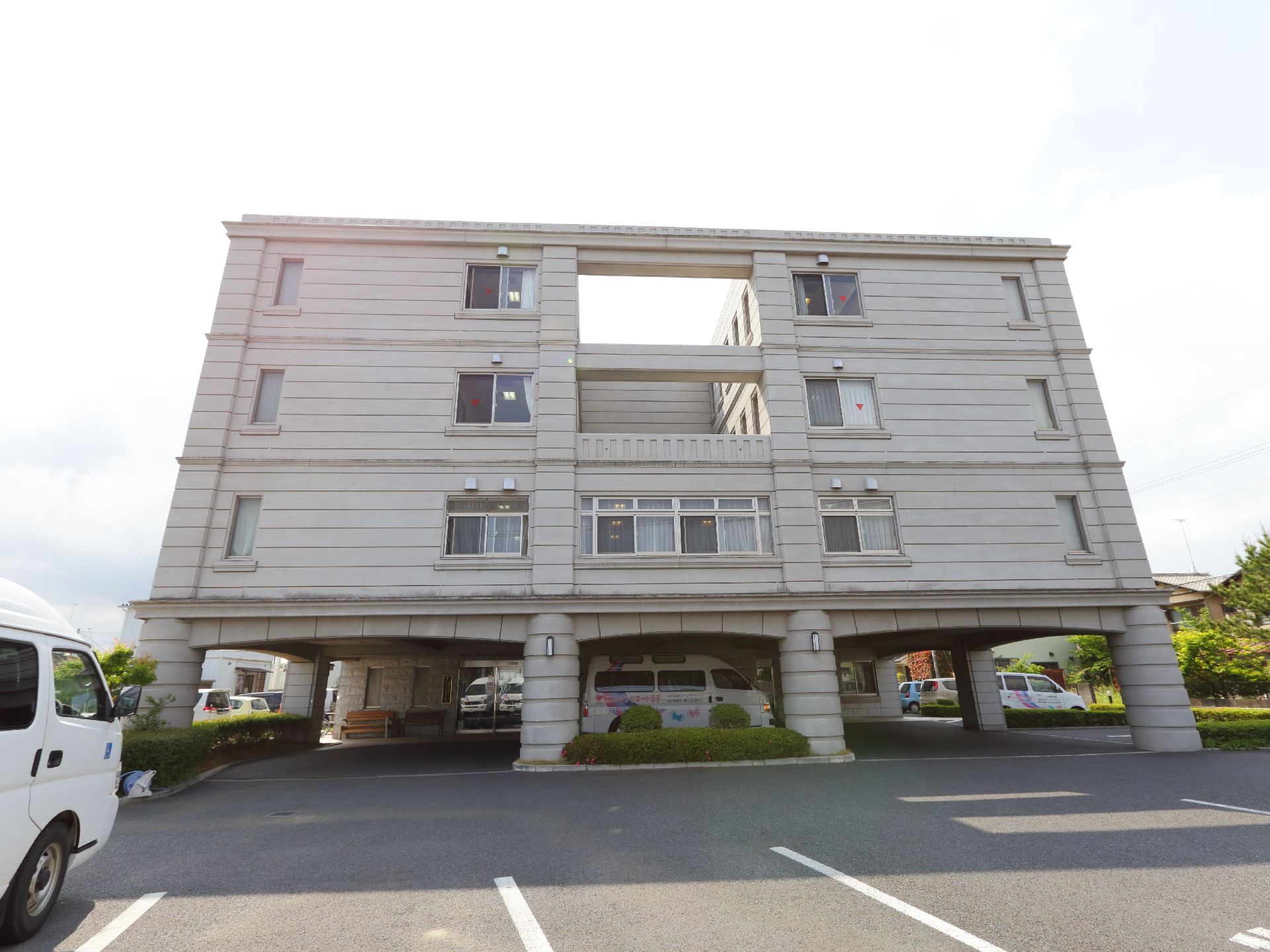 施設の外観は、白い外壁で統一されている。1階部分は半分程が玄関前の車が横付けできるスペースが確保されている。