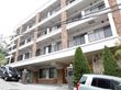 白と茶色でまとめられた4階建ての外観である。手前の道路は少し坂道になっていて、道路わきに2台の車が置いてある。