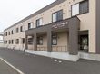 施設の外観はグレーとベージュの色の外観になっている。シンプルなマンションのような形で、建物には施設名が書かれている。