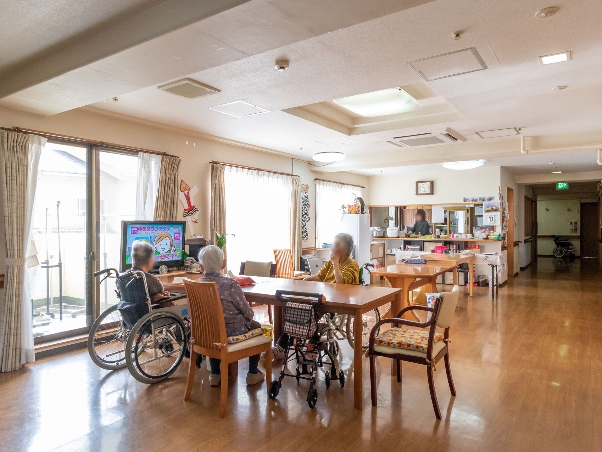テレビ、テーブル、椅子などが並べられている。テーブルには複数の人物がいて、テレビを見ながら憩いのひと時を過ごしている。