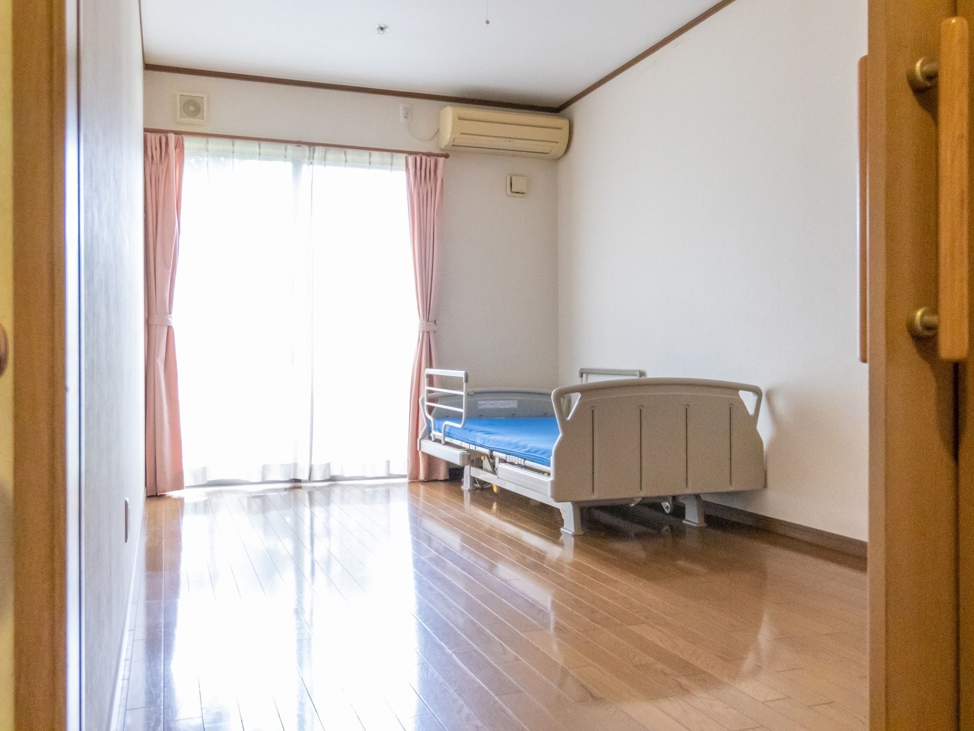奥にある窓から日が良く入り、居室内は明るく親しみやすい雰囲気になっている。窓際にベッドが配置され、室内は広々としている。