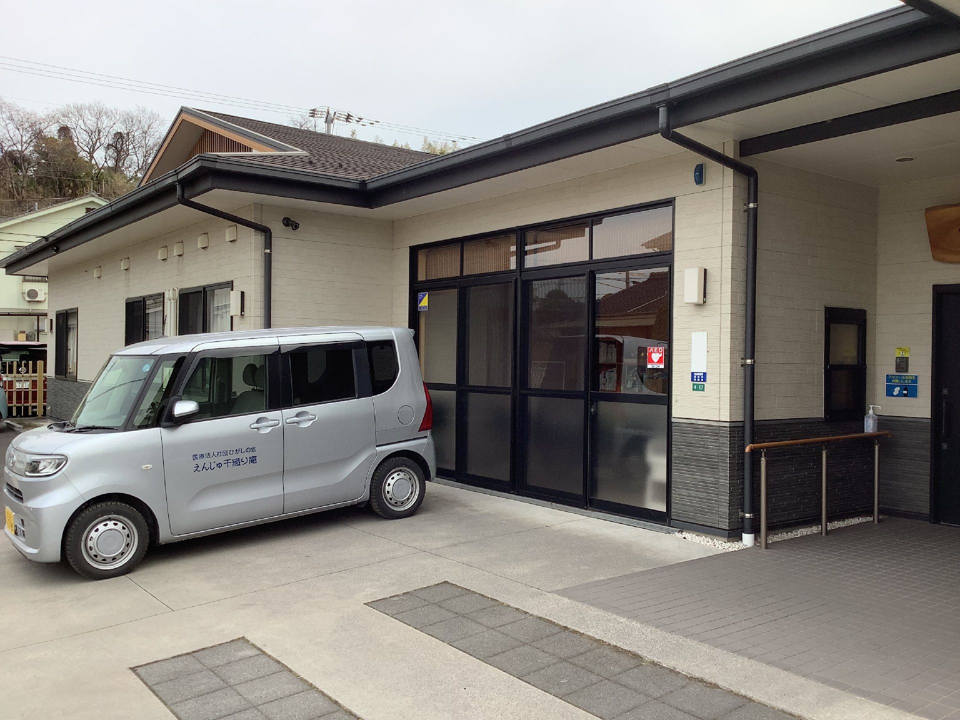 シルバーの車が建物の前に泊まっている。建物は平屋建てで、大きな窓が付いている。