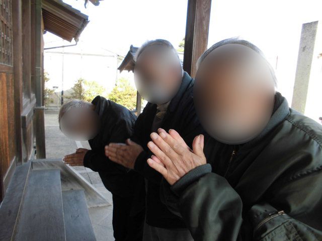 ピンクのエプロンを付けた若い女性スタッフがカーディガンを着た車いすの高齢女性に寄り添い、微笑んでいる。