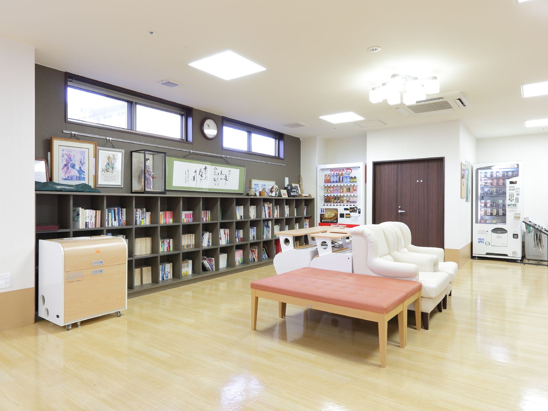 壁一面の本棚に、たくさんの本が並んでいる。自動販売機が2台あり、新聞ラックもある。ベンチが置かれている。