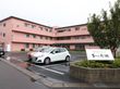 3階建てとなっている施設外観の手前には駐車場があり、何台かの車が止まっている。入り口には看板がある。