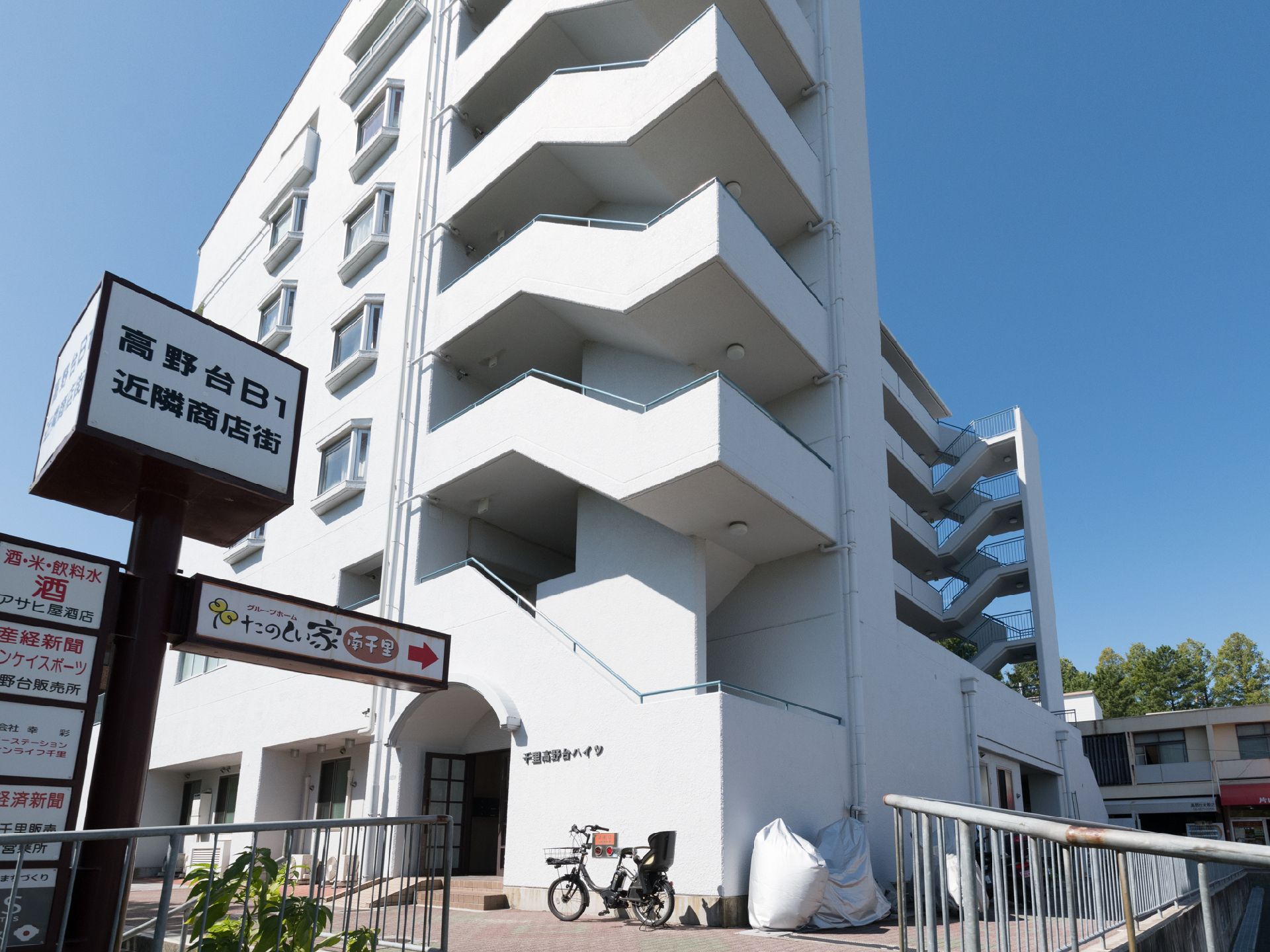 施設の入り口付近を外から撮影した画像である。画像の左側には、施設周辺の店舗情報が載った案内板が設置されている。