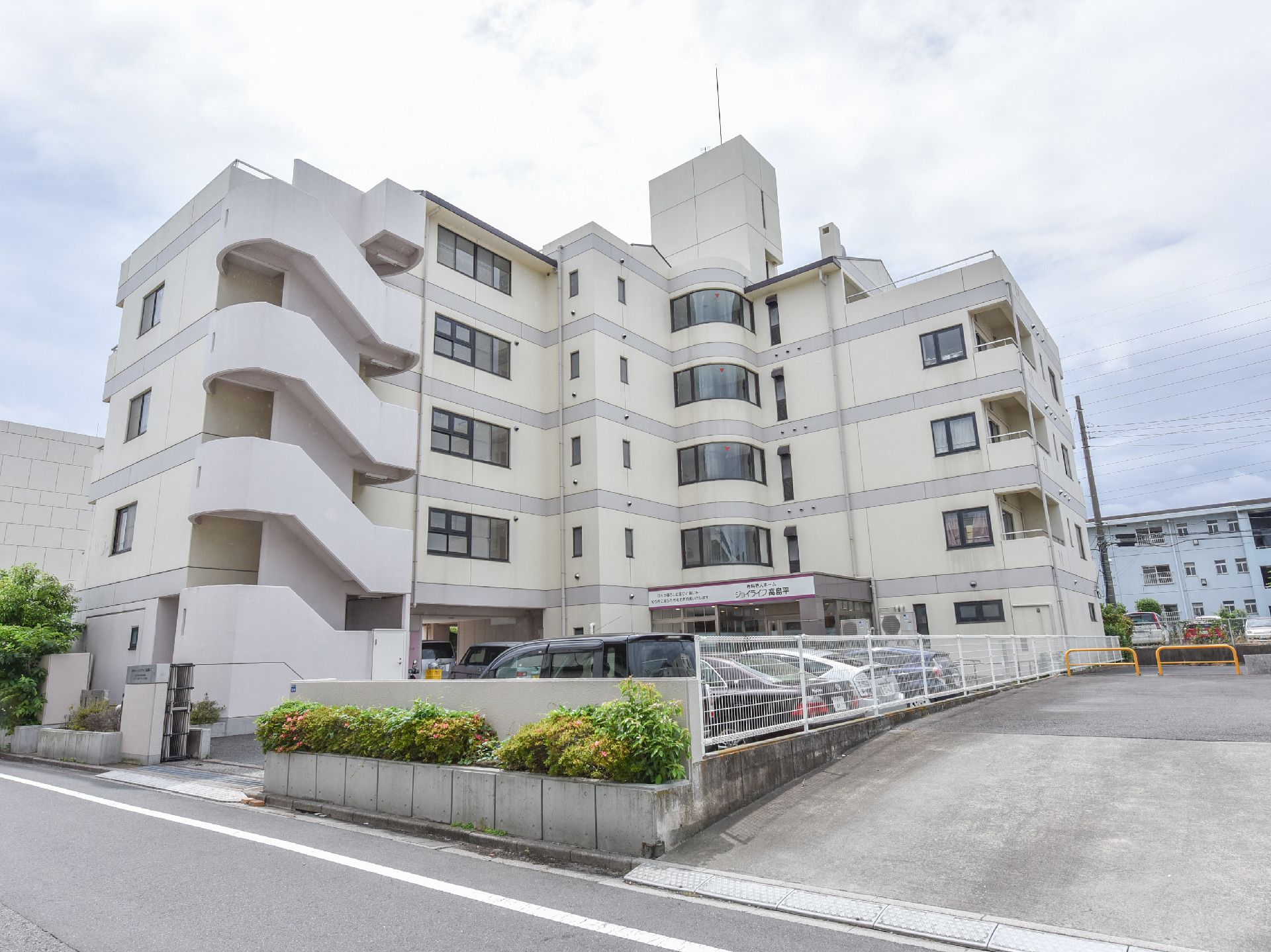 陽当たりの良い道路に面した4階建ての建物。周りはコンクリートできれいに整備され、駐車場も敷地内にある。