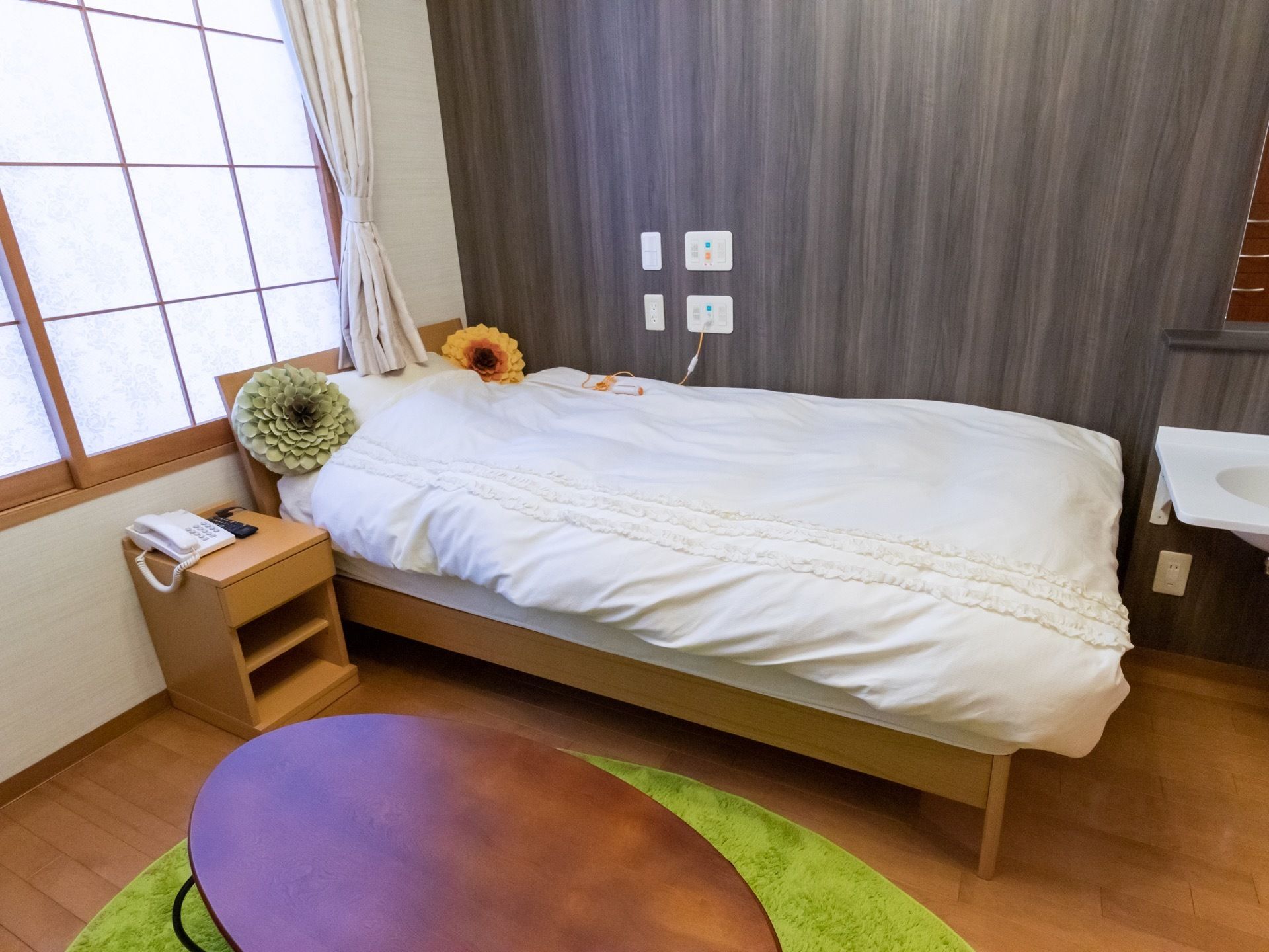 居室にはベッドやテーブルなどが置かれており、壁にはナースコールがある。窓には障子とカーテンがかかっている。